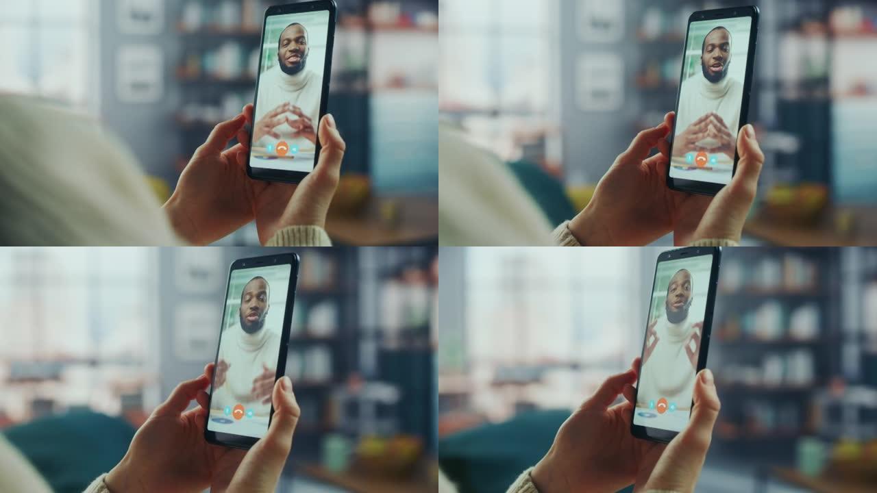 一名女性在家庭客厅的智能手机上与她英俊的非裔美国男性朋友在视频通话中聊天的特写镜头。自由职业者通过互