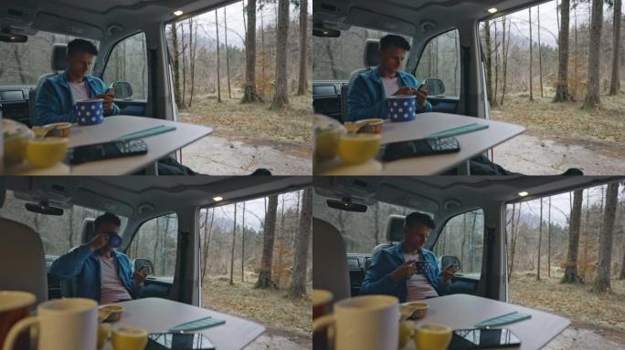 棕色短发的男人坐在他的货车里，用智能手机，端着他的咖啡喝，早餐桌在他面前