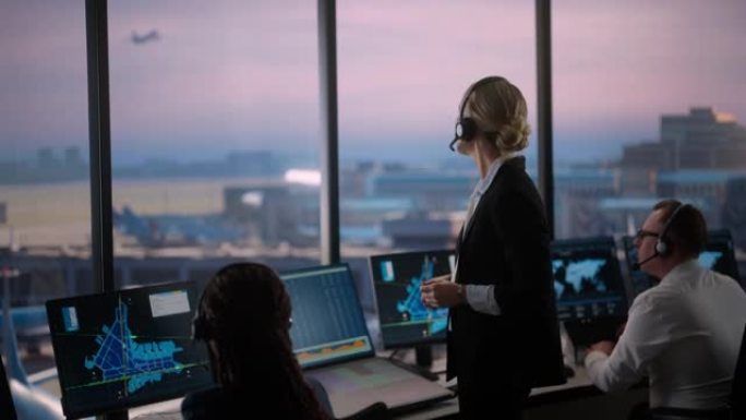 戴着耳机的女性空中交通管制员在机场塔楼通话。办公室里满是台式电脑显示屏，配有导航屏幕，飞机飞行雷达数