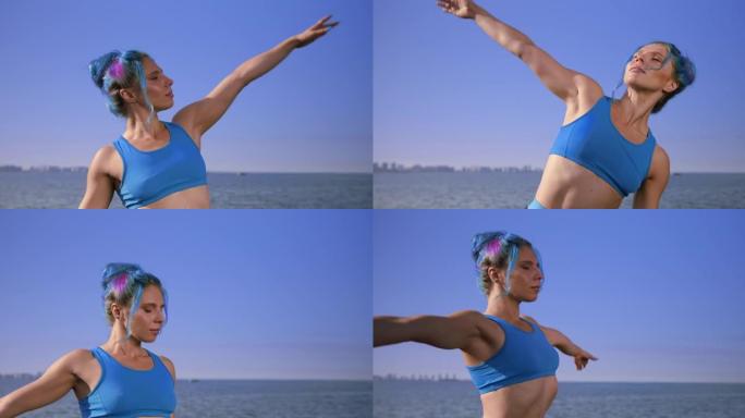 迷人的健身瑜伽老师，绿松石色的运动上衣中的绿松石色头发站在天空和大海的背景下，展示了肩膀的一些伸展动