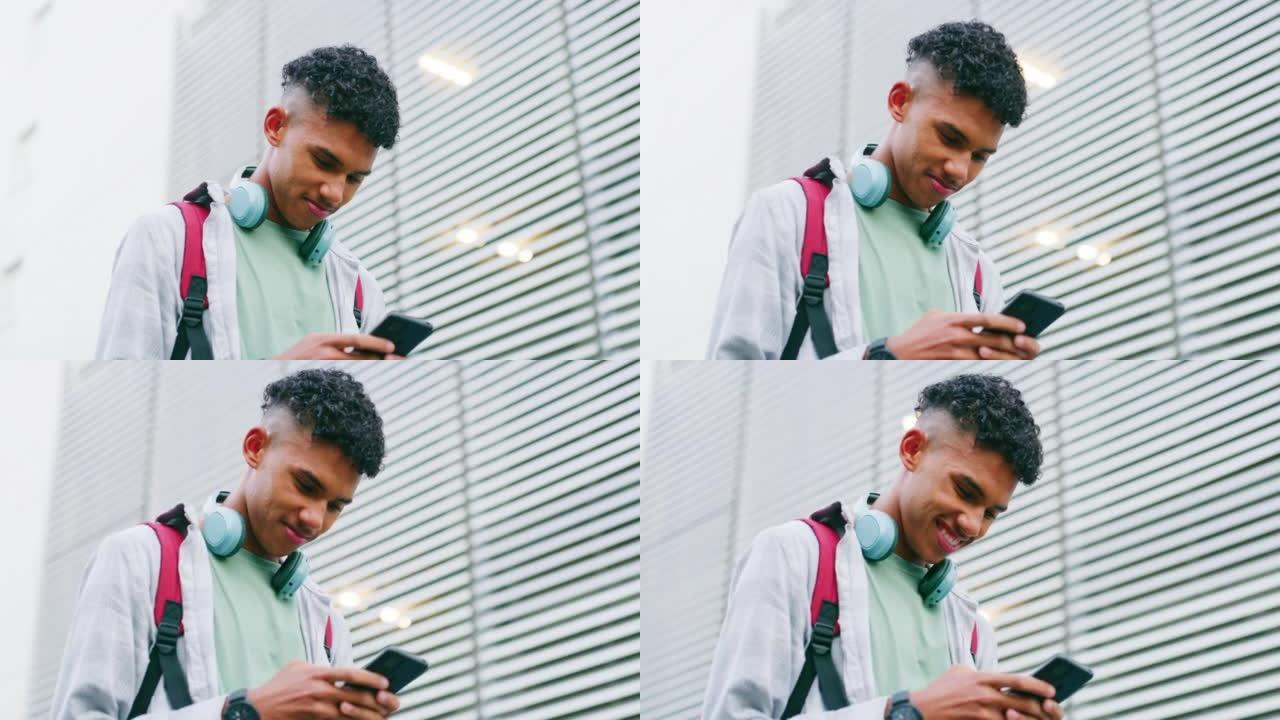 一个年轻人在外面用电话聊天和观看视频的低角度。带着蓝牙耳机的快乐男学生看着他的屏幕，在一座高楼旁边发