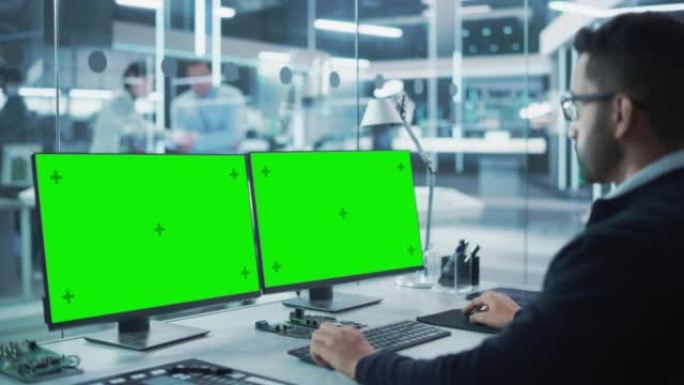 软件开发人员在工厂中使用带有两个绿屏Chromakey显示屏的台式计算机上工作。现代技术研发中心。