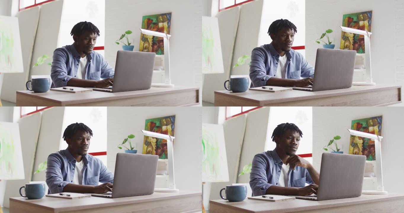 体贴的非裔美国男艺术家坐在艺术工作室的桌子上使用笔记本电脑