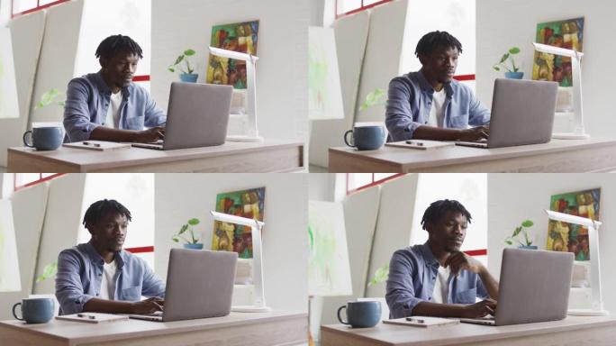 体贴的非裔美国男艺术家坐在艺术工作室的桌子上使用笔记本电脑