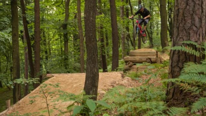 山地自行车手下坡加速，在泥泞的小径上跳跃，表演特技称为自行车鞭，背景为绿色森林