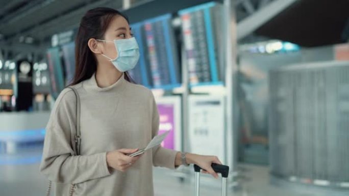 年轻的女旅行者戴着外科口罩，在电子时刻表上检查登机时间
