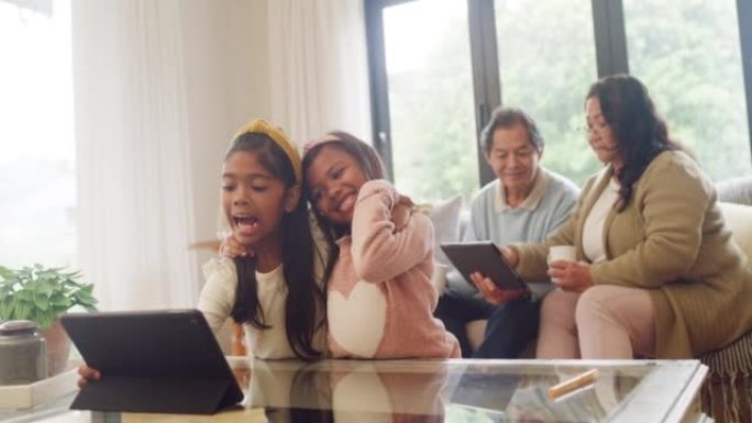 女孩们在客厅里玩数字平板电脑，祖父母照看孩子。快乐傻姐妹拉脸自拍奶奶爷爷在沙发上聊天