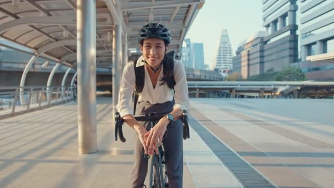 亚洲女商人去办公室工作，穿着微笑的背包，在城市周围的街道上，用自行车看着相机。