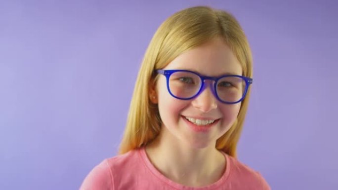 在紫色工作室背景下戴着蓝色眼镜的长发微笑女孩的工作室拍摄-慢动作拍摄