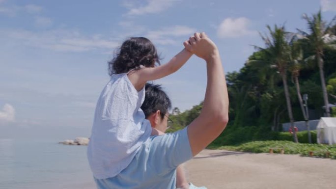 亚洲父亲一边在沙滩上玩耍，一边把女儿扛在肩上