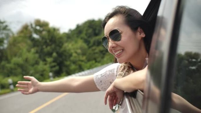 亚洲妇女将手伸出车窗，微笑着。慢动作