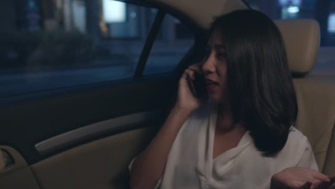穿着时尚办公服装的亚洲女商人深夜在城市现代城的汽车后座上聊天智能手机。