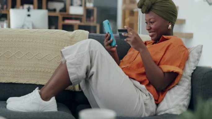 信用卡，智能手机和黑人妇女在线购物支付在她的家庭沙发上兴奋的在线商店销售，促销或折扣。女人使用手机进