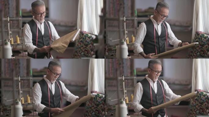 工作室亚洲中国成熟男子裁缝脸茬检查他的面料服装工作室
