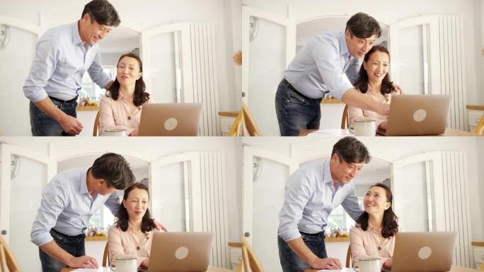 成熟的亚洲男人在家里给妻子带来咖啡，他们一起用笔记本电脑检查家庭账单 -- 慢动作拍摄