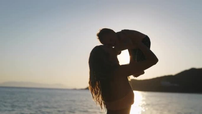 一位年轻的neo母亲的真实特写镜头保持在她的手臂上，并在海边的海滩上与新生婴儿玩耍