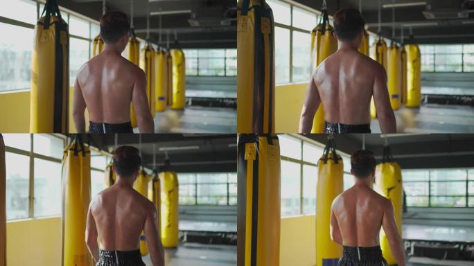 后视亚洲中国男运动员在健身房健身俱乐部散步，窗户旁边有一排黄色沙袋