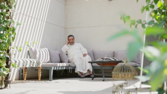 50年代末的沙特男子在阳光明媚的露台上使用电话