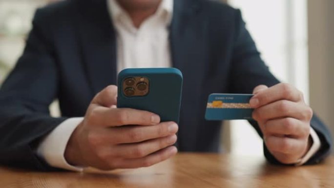 男子手持信用卡和手机在线购物特写。持有智能手机并使用网上银行支付的客户。概念在线支付坐在家里。商店应