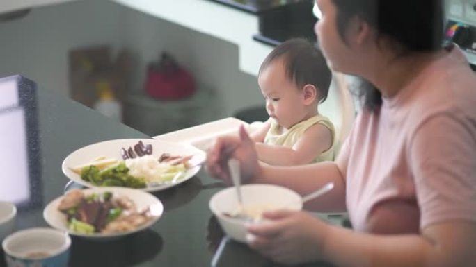 亚洲婴儿与母亲在厨房吃午餐