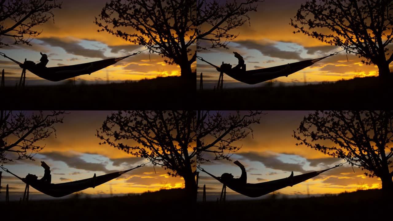 日落时在吊床上看书的女人的SLO MO剪影