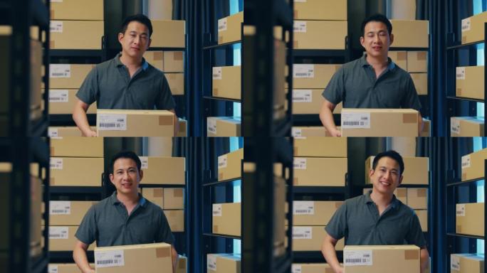 成功的亚洲商人站在货架前，拿着纸板纸盒微笑着看着相机，自豪地展示了他晚上在仓库里的生意。