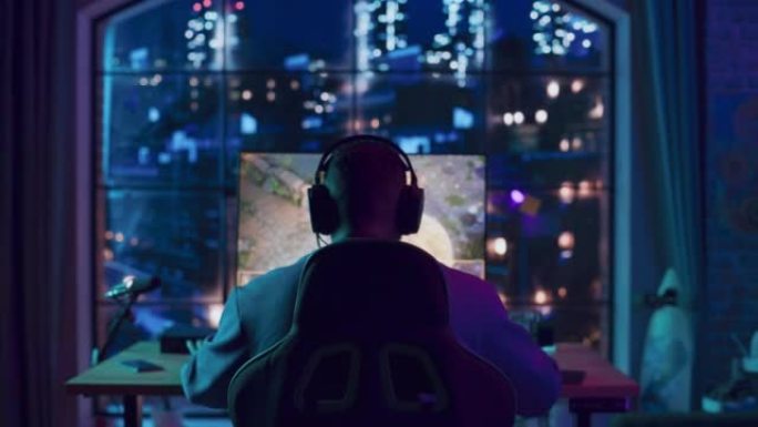 一个成功的非洲裔美国玩家戴上耳机，在家里霓虹灯照明的客厅里用个人电脑玩视频游戏的后角。胜利的年轻人。