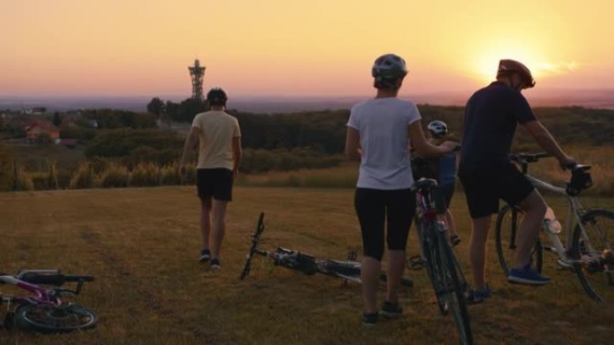 SLO MO家庭有三个孩子骑自行车，当他们停在草地上时，可以看到远处的塔Vinarium