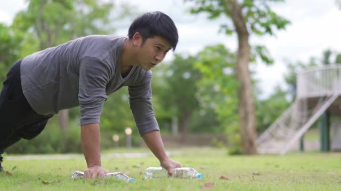 亚洲男子在公园用水瓶锻炼胸部运动