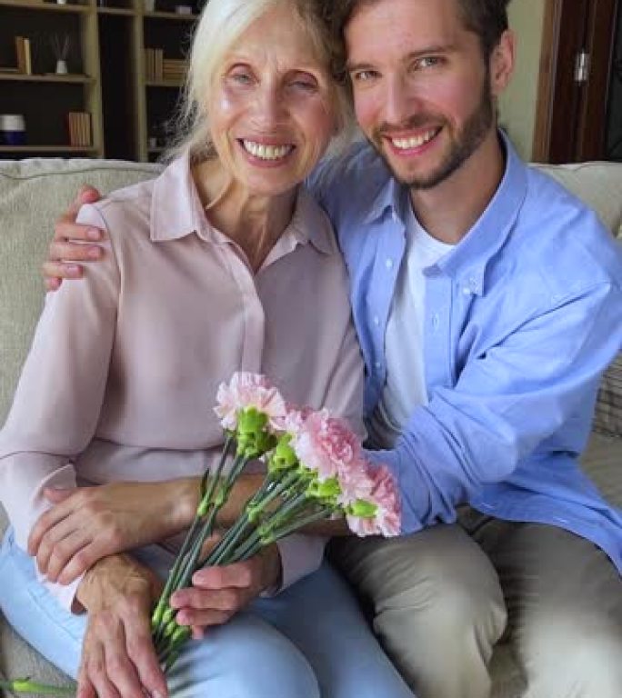 垂直视图快乐大人儿子拥抱年长的妈妈拿着花