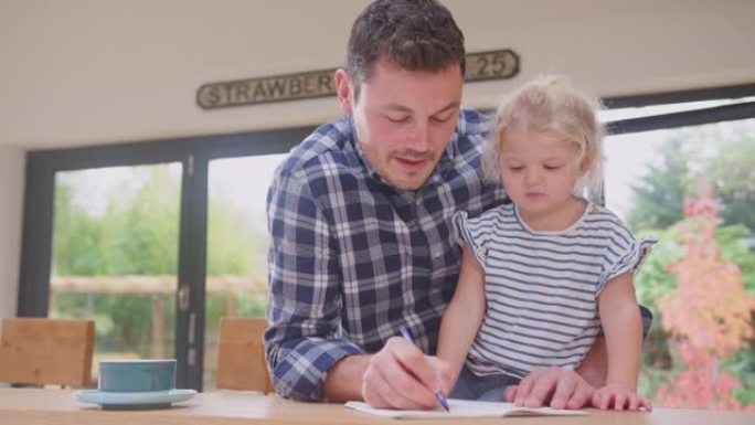 父亲在家在厨房柜台帮助小女儿在书上画画