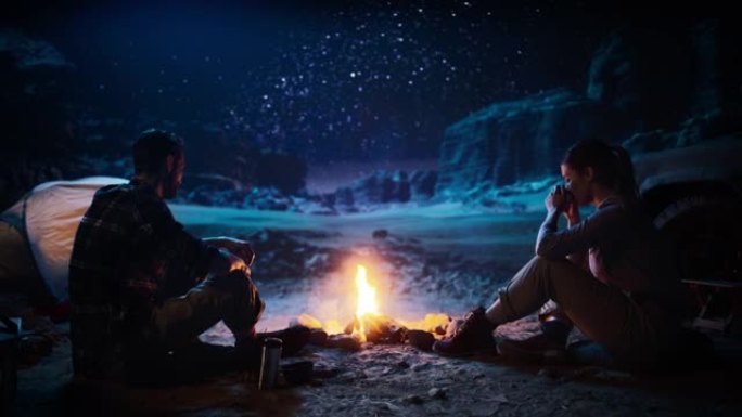 快乐的夫妇坐在篝火旁，在峡谷露营时看着夜空。两个旅行的人在露营地讲鼓舞人心的故事，看看银河系的星星。