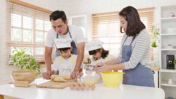 快乐微笑的年轻亚洲日本家庭与学龄前儿童有乐趣烹饪烘焙糕点或馅饼在早上的现代厨房家庭早餐。