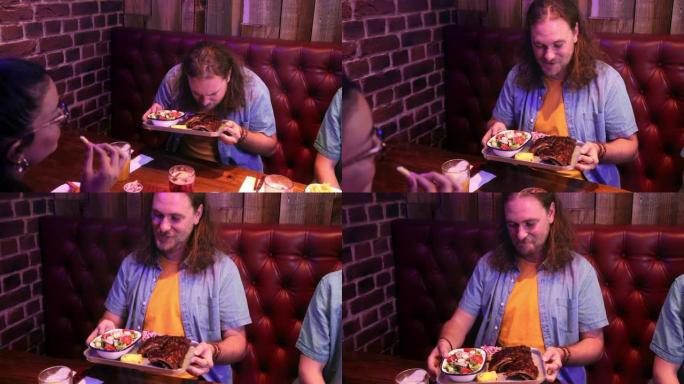男人在餐厅和朋友一起拿着一盘烧烤排骨