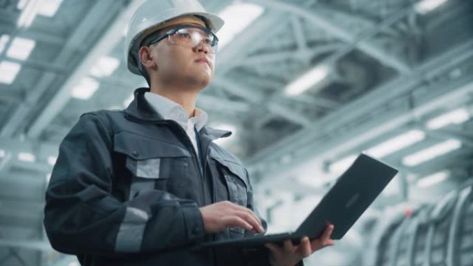穿着安全制服和安全帽的专业重工业亚洲工程师/工人的肖像使用笔记本电脑。自信的中国工业专家站在工厂里。
