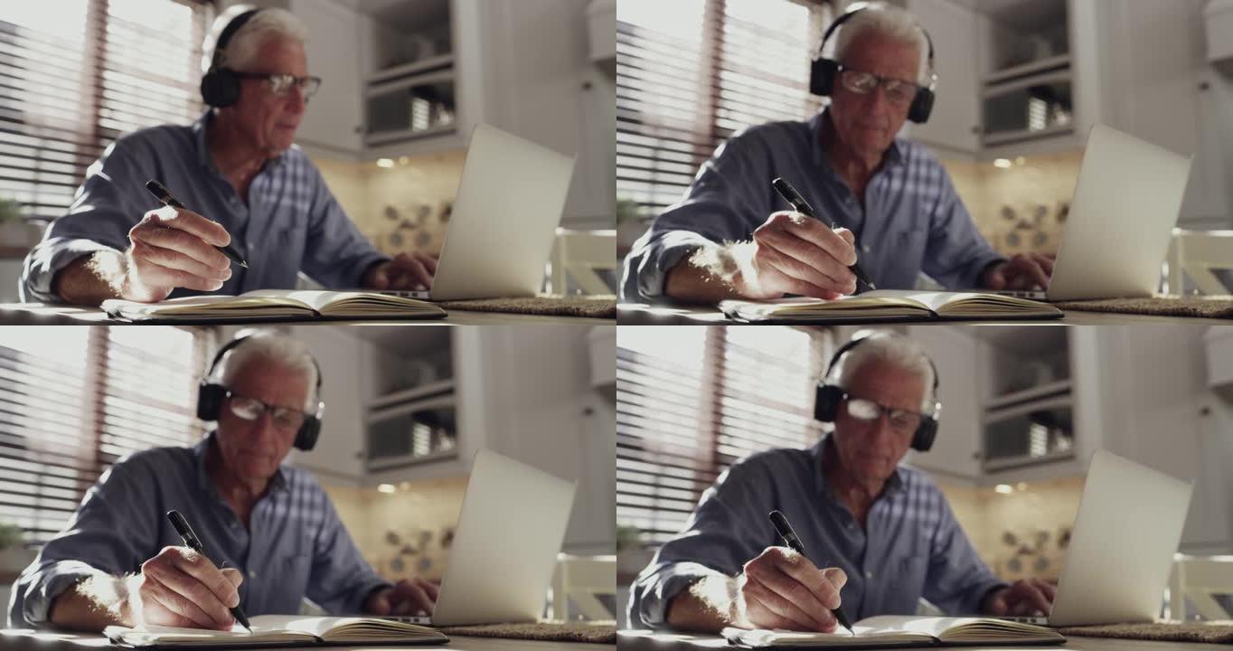 4k视频片段，一名高级男子独自坐在家里的厨房里，并在使用技术时戴着耳机