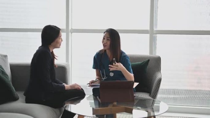 亚洲华裔女医生在办公室沙发上向一名女患者解释医疗报告