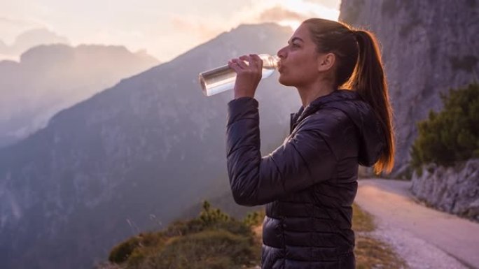 在山坡上的女人被慢慢夕阳照亮，用水瓶喝水