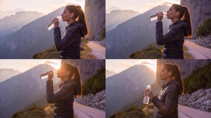 在山坡上的女人被慢慢夕阳照亮，用水瓶喝水