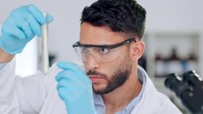 一位年轻的专业男性科学家在实验室里看着试管。药剂师学生在covid大流行期间在实验室检查液体。测量调