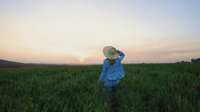 慢动作特写后视图一名戴着草帽的美丽年轻女子在日落时在麦田里奔跑和跳跃