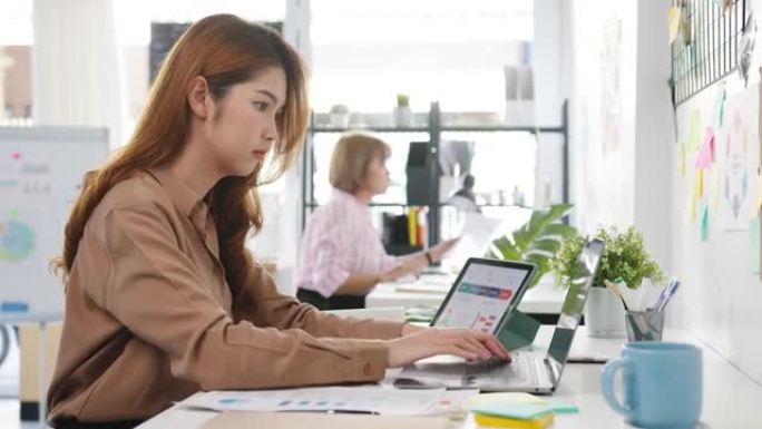 年轻的亚洲女商人企业家在新的正常情况下进行社会距离，以预防病毒，同时在办公室工作时使用笔记本电脑和平