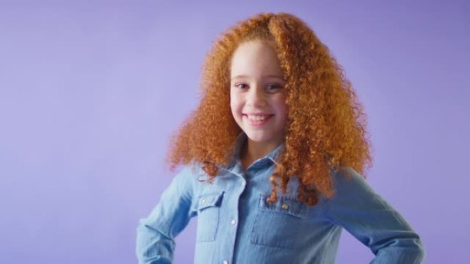 工作室拍摄的红头发微笑女孩站在紫色背景下，双手放在臀部 -- 慢动作拍摄