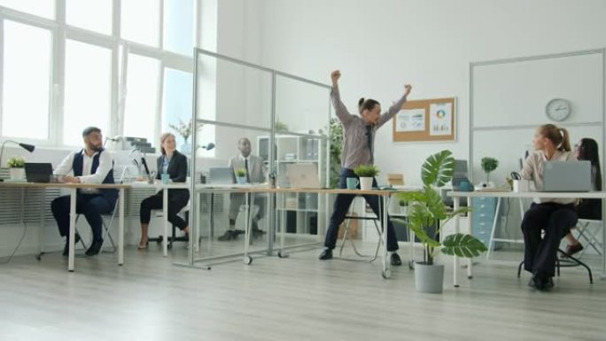 商人在办公室工作，然后在同事鼓掌的同时获得好消息跳舞