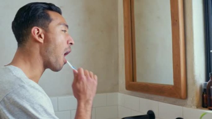 浴室镜子里有牙刷的人，用于牙齿健康、健康或口腔卫生或护理。年轻的亚洲男性早上在家用刷子清洁牙齿，以美