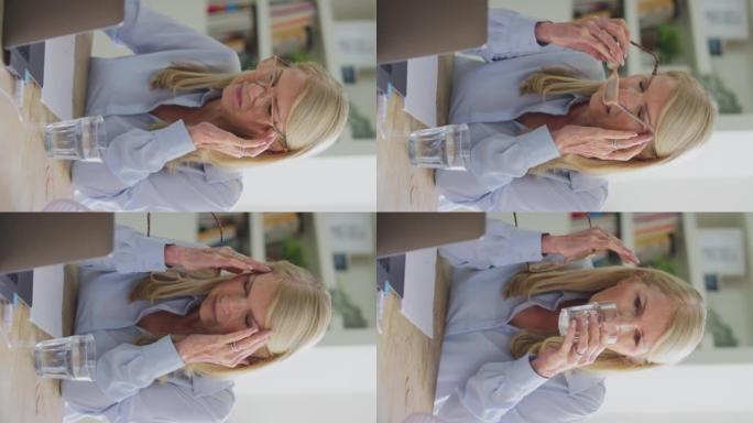 更年期成熟妇女戴眼镜在笔记本电脑上工作的垂直视频，在慢动作中头痛