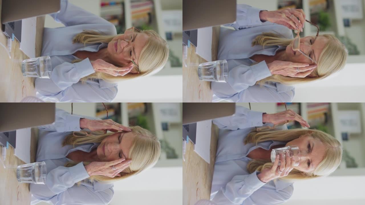 更年期成熟妇女戴眼镜在笔记本电脑上工作的垂直视频，在慢动作中头痛