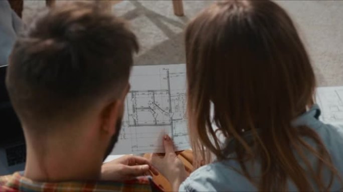 梦见新家。年轻幸福的夫妇在地板上吃披萨，看着新的公寓规划蓝图规划未来。