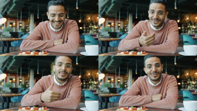 英俊的阿拉伯男子在咖啡馆里聊天，挥舞着手笑着看着相机