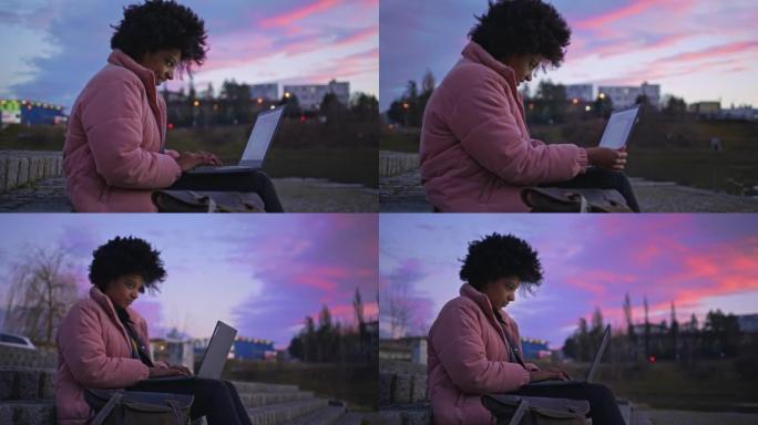 快乐的年轻女子坐在楼梯上使用笔记本电脑在城市公园黄昏